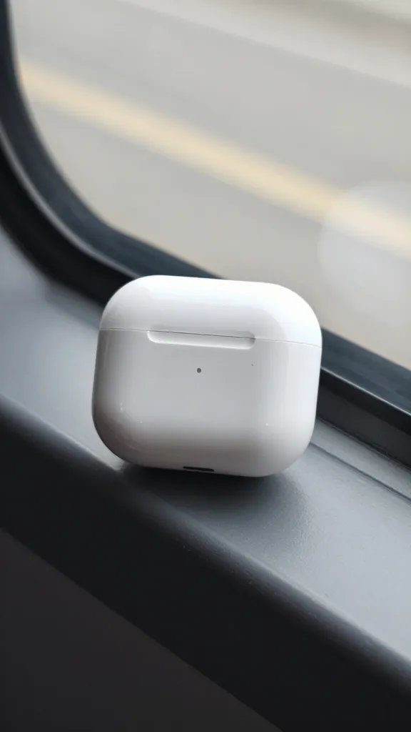 closeup of a glass window with a single white noise-canceling earbuds case on sill
