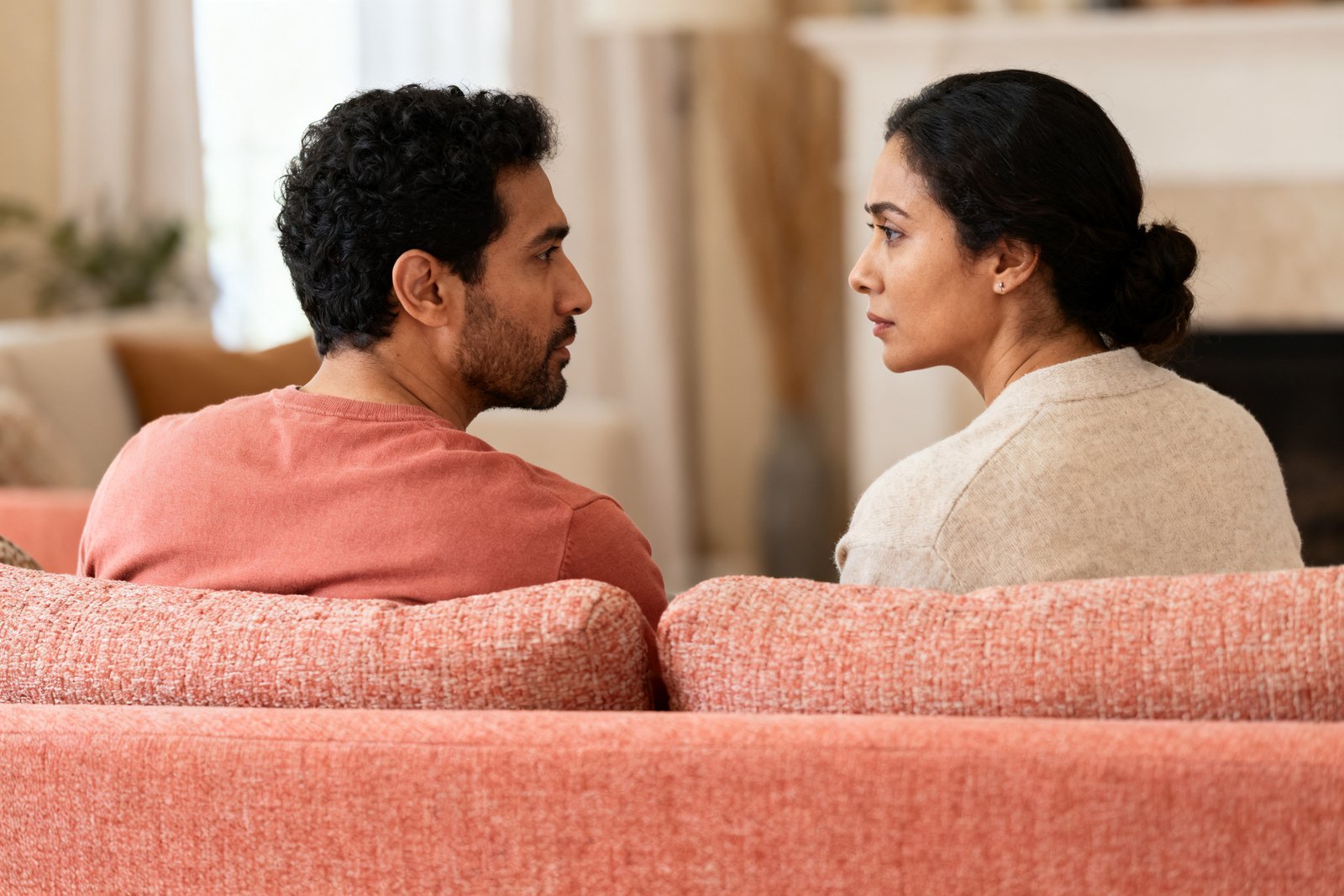 A couple sitting calmly and close on a living-room sofa having a gentle but serious conversation, facing each